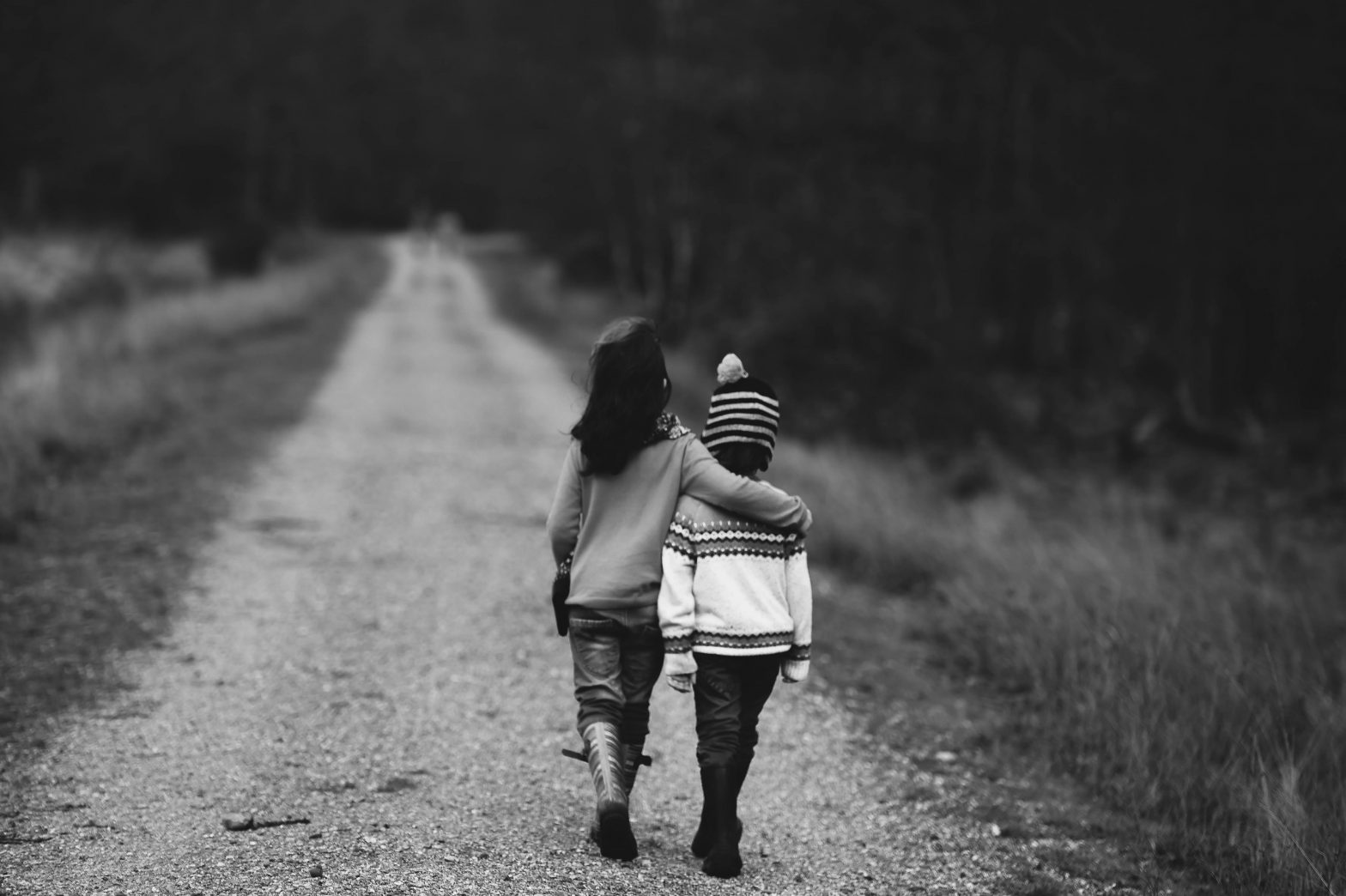 Two kids walking down a dirt road; one with their arm around the other.